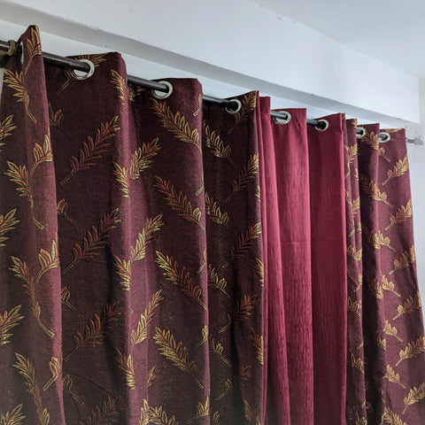 Maroon curtains with gold leaf pattern hanging on a white wall.