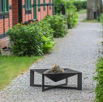 Black metal fire pit on a gravel pathway with greenery and a building in the background