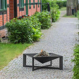 Black metal fire pit on a gravel pathway with greenery and a building in the background