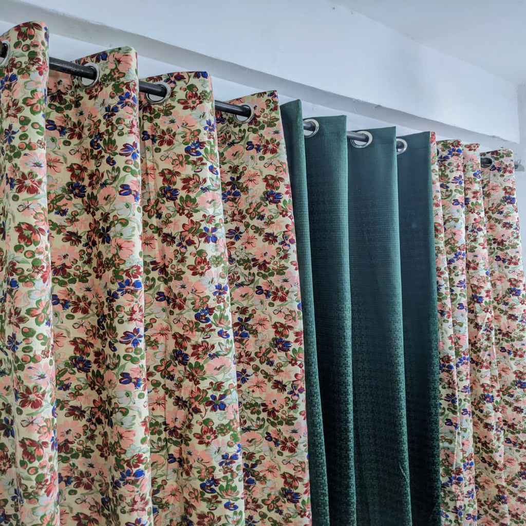 Floral and solid color curtains hanging on a rack against a white wall.