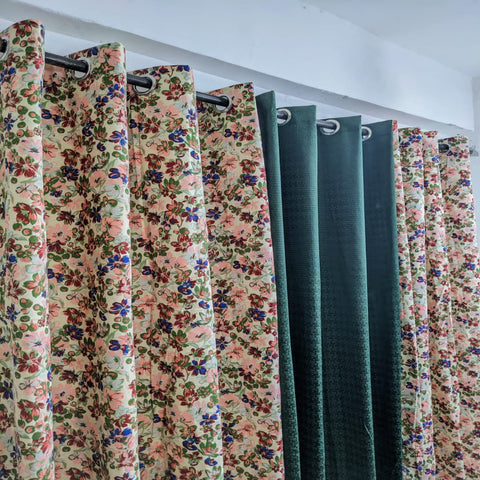 Floral and solid color curtains hanging on a rack against a white wall.