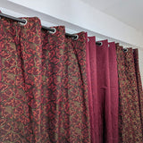 Red patterned curtains hanging from a rod against a white wall.