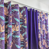 Set of purple floral curtains hanging on a rod against a white wall.