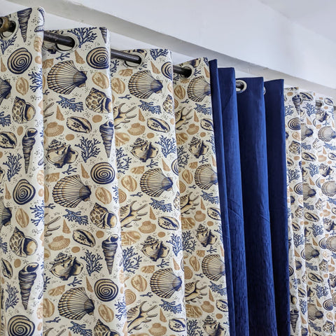Curtains with shell pattern and solid blue color hanging on a rod.