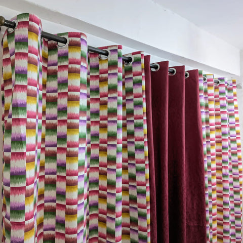 Colorful patterned curtains hanging on a rod against a white wall.