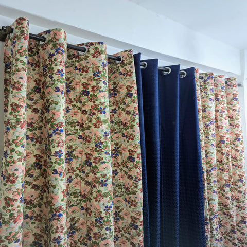 Floral patterned curtains and a solid blue curtain hanging on a rod against a white wall.