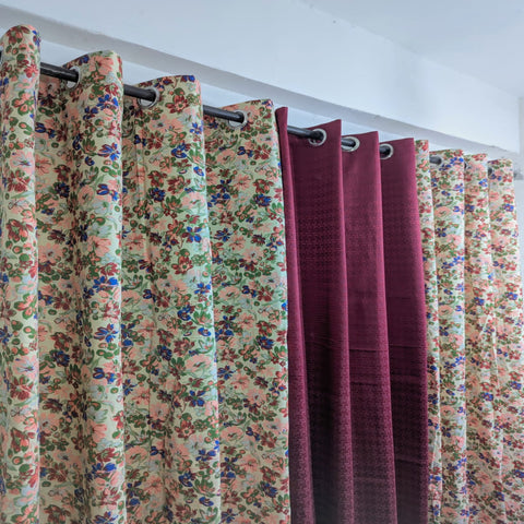 Set of floral and solid color curtains hanging on a rod against a white wall.