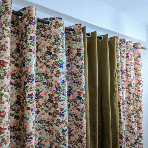 Floral and solid color curtains hanging on a rod against a white wall.