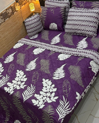 Purple bedspread with leaf patterns on a bed in a bedroom setting.